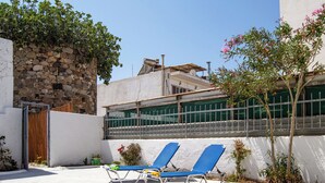 A courtyard with two blue lounge chairs, a stone wall, and a metal fence. - The Three Sisters House (Kardamena)