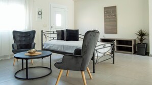 A modern bedroom with a bed, two chairs, a small round table, and a potted plant. - The Three Sisters House (Kardamena)