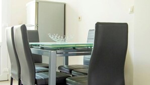 A dining area with a glass-top table, black chairs, and a white cabinet in the background. - The Three Sisters House (Kardamena)
