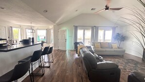 A spacious living area with a long leather sofa, a dining area with bar stools, and a kitchen with a large island. - Cozy Beach House - short walk to the water, quiet neighborhood. (Galveston)