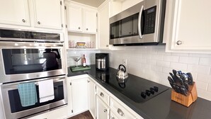 A modern kitchen with stainless steel appliances, white cabinetry, and a black countertop. - Cozy Beach House - short walk to the water, quiet neighborhood. (Galveston)