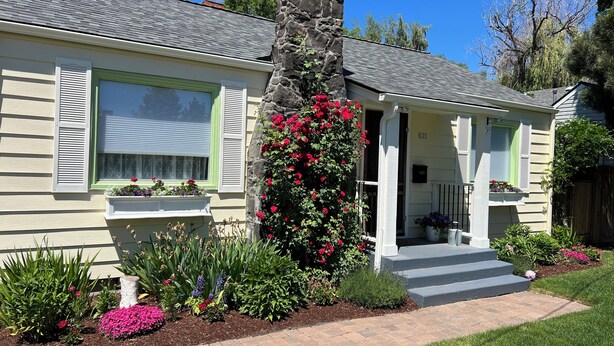 A single-story house with a stone pillar, a front porch, and a well-maintained garden with various flowers and shrubs. - Cozy Cottage in Downtown Redmond (Redmond)