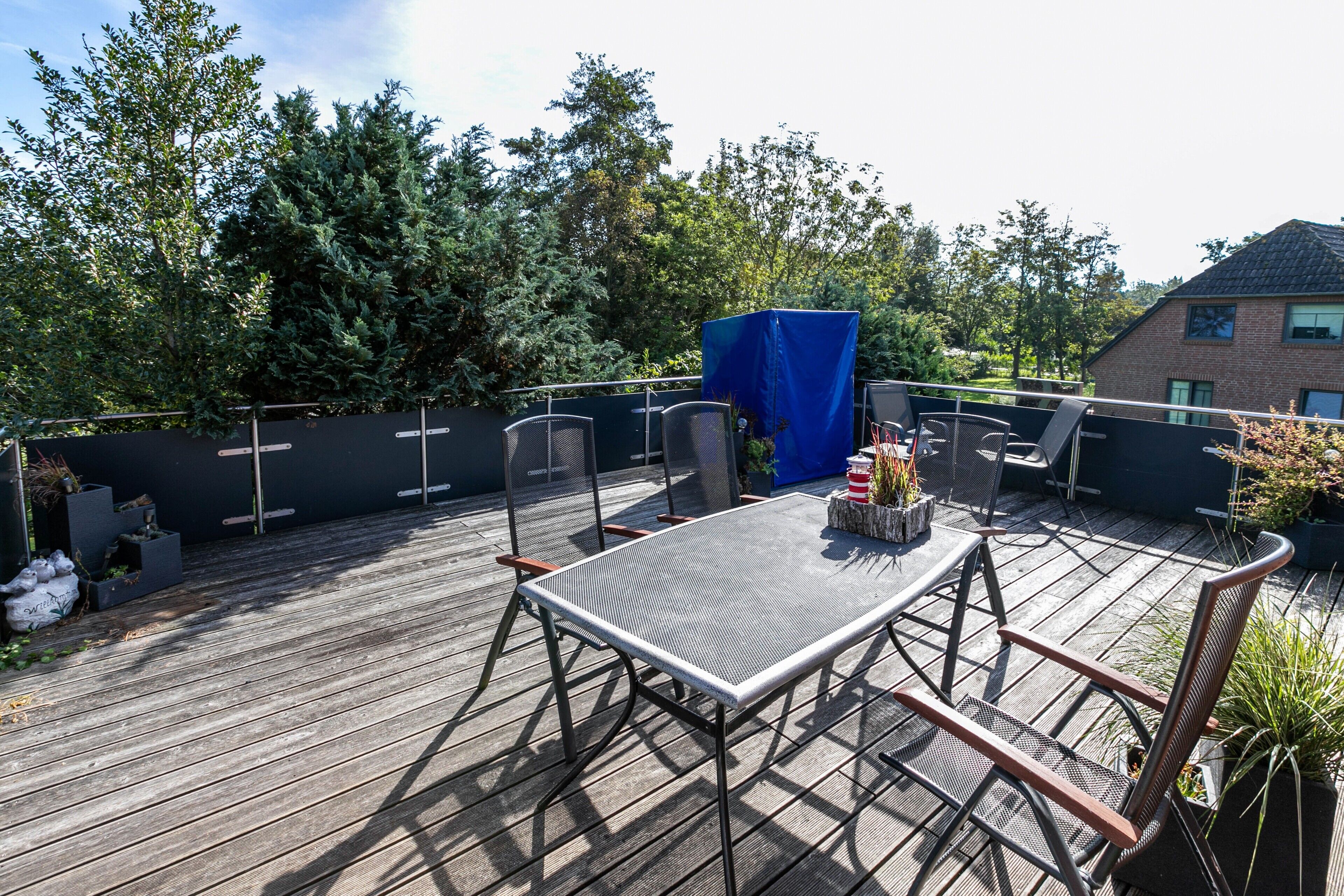 A wooden deck with a table and chairs, surrounded by a fence and trees.