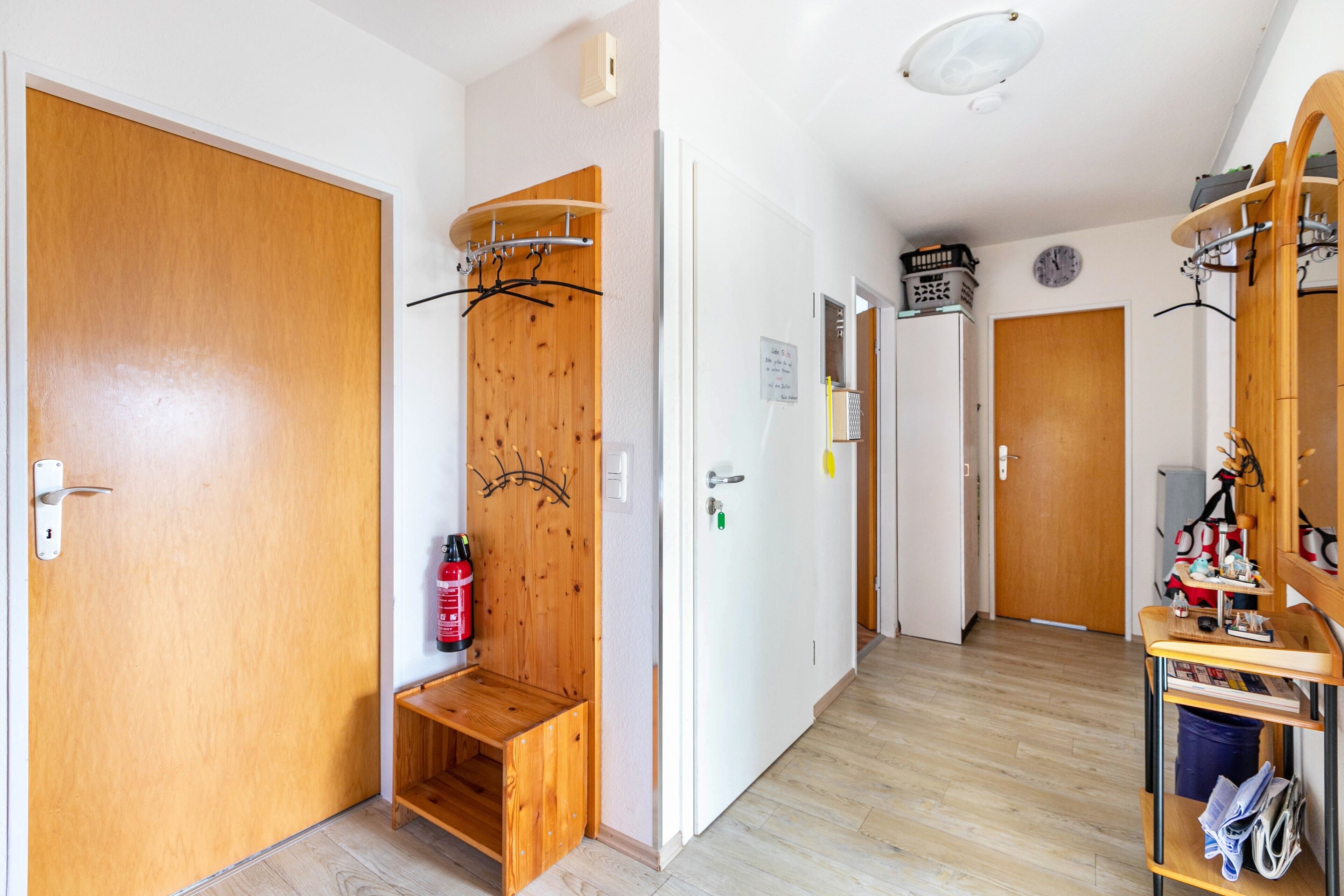 Un pasillo con puertas de madera, un extintor, un perchero y un pequeño banco de madera.