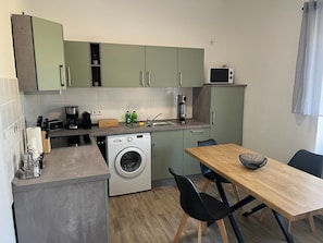A compact kitchen with a washing machine, a microwave, and a dining area with chairs and a table. - Apartment "2 - Haus Lausitzring" with Private Terrace & Wi-Fi (Annahütte)