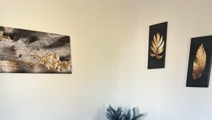 Un salon moderne avec un canapé gris foncé, une table basse en bois agrémentée d’un arrangement floral blanc, un pouf rond noir et deux œuvres d’art représentant des feuilles, encadrées et accrochées au mur.
