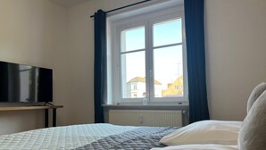 Une chambre d’hôtel avec un lit, un téléviseur posé sur un meuble, une fenêtre avec des rideaux et un radiateur.