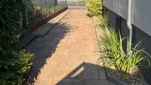 Un chemin pavé mène à un quartier résidentiel où se trouvent des maisons, une clôture en métal et de la verdure.