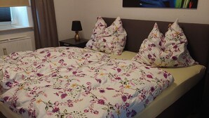 Un lit avec une literie à motifs floraux, une table de chevet avec une lampe et un tableau accroché au mur.