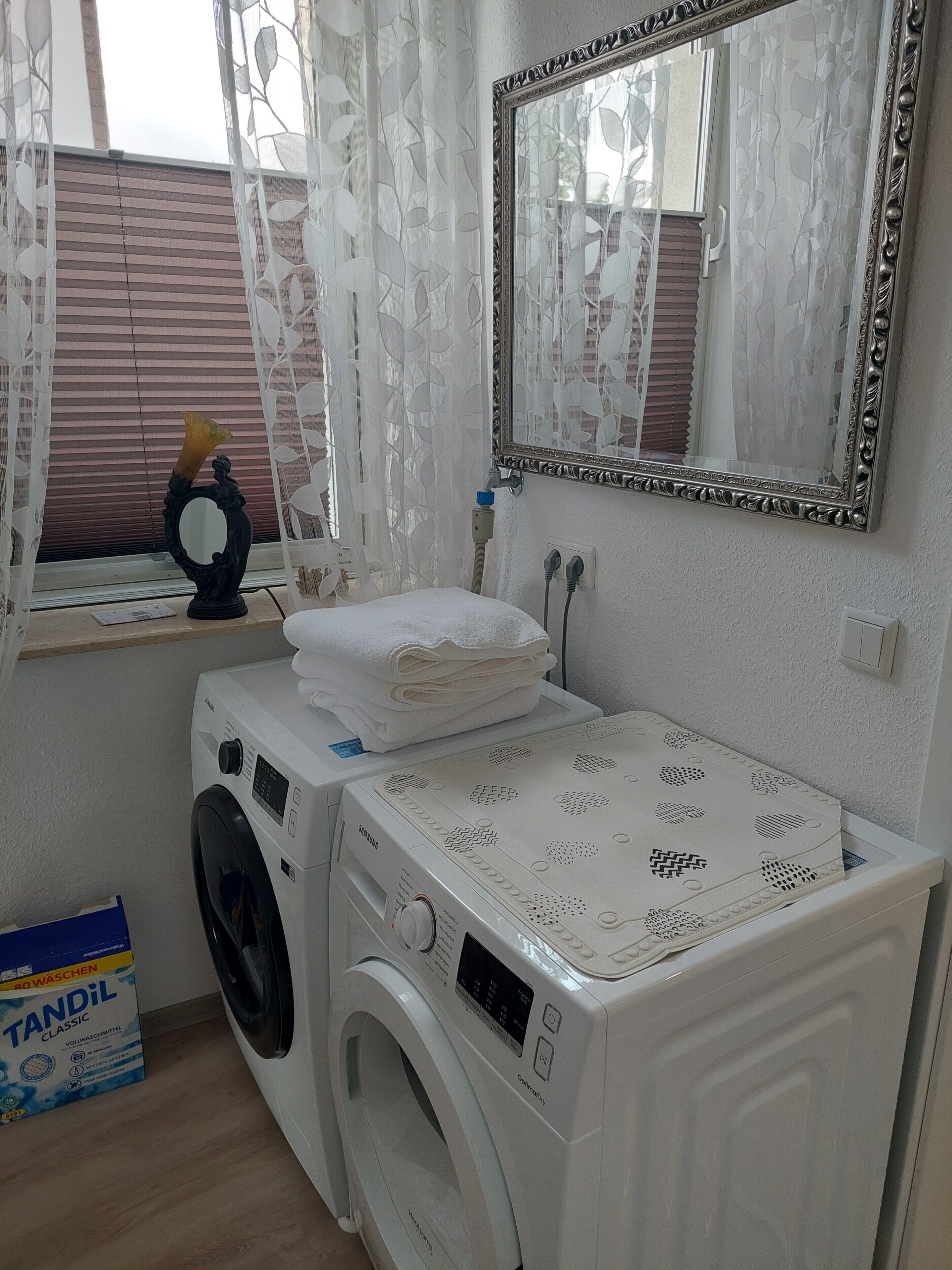 Een wasserette met een wasmachine, een droger, een spiegel en een raam met zonwering.
