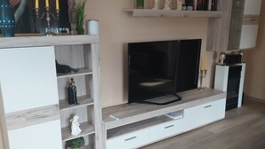 Un salon moderne doté d’un téléviseur à écran plat, d’étagères en bois, d’objets décoratifs et d’un sol recouvert de moquette.