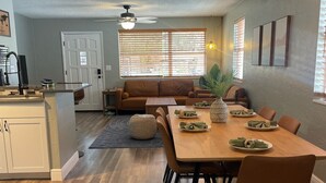 A modern living room with a brown leather sofa, a dining table set for four, and a kitchen area with white cabinetry. - Unleash the Fun: Pool Table, Fishing Poles, and Ping Pong Table, Smoker (Port Orange)