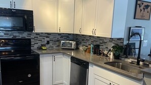 A modern kitchen with white cabinets, a black microwave, a toaster, and a dishwasher. - Unleash the Fun: Pool Table, Fishing Poles, and Ping Pong Table, Smoker (Port Orange)
