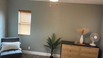 A room with a ceiling fan, a window with blinds, a dark-colored sofa, a wooden dresser, and a potted plant.