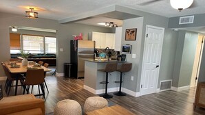 A modern kitchen with a central island, bar stools, and a dining area with a wooden table and chairs. - Unleash the Fun: Pool Table, Fishing Poles, and Ping Pong Table, Smoker (Port Orange)