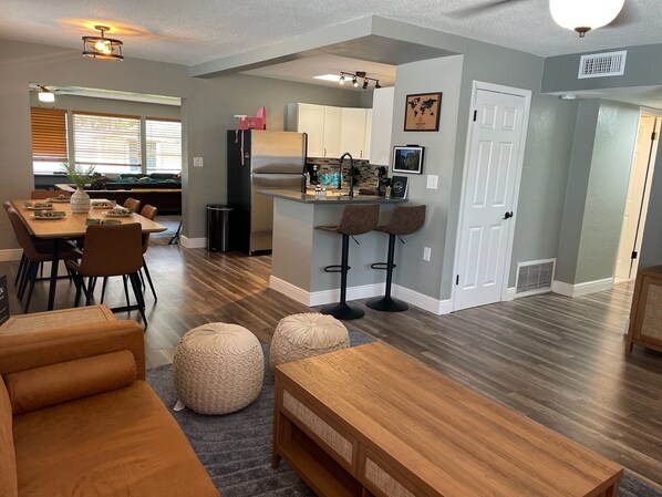 A modern kitchen with a central island, bar stools, and a dining area with a wooden table and chairs.