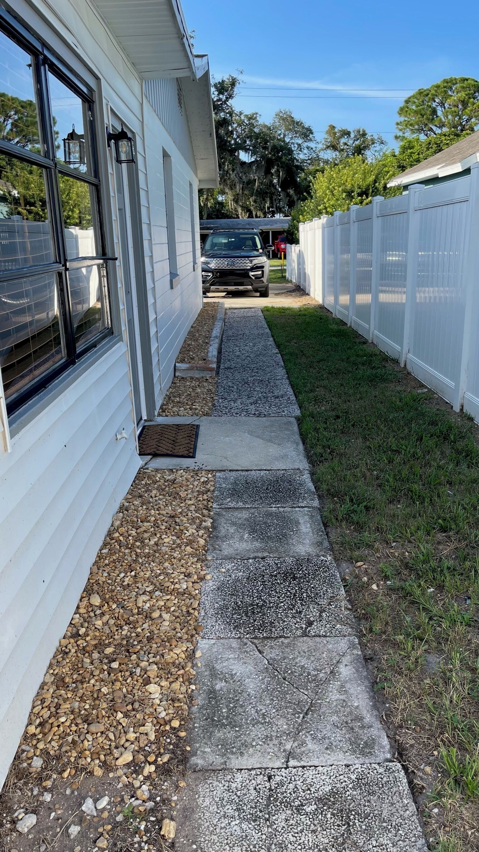 Un vialetto conduce a una casa con un garage, circondata da un recinto bianco e un prato.