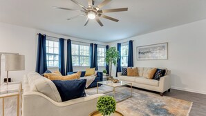 A modern living room with a ceiling fan, two sofas, a coffee table, and a large window with curtains. - Elegant Atlanta Home - Self Check-in (Atlanta)