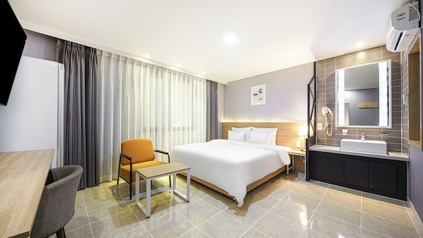 A hotel room with a bed, a desk, a chair, a bathroom with a sink and mirror, and curtains. - Browndot Angang (Gyeongju)