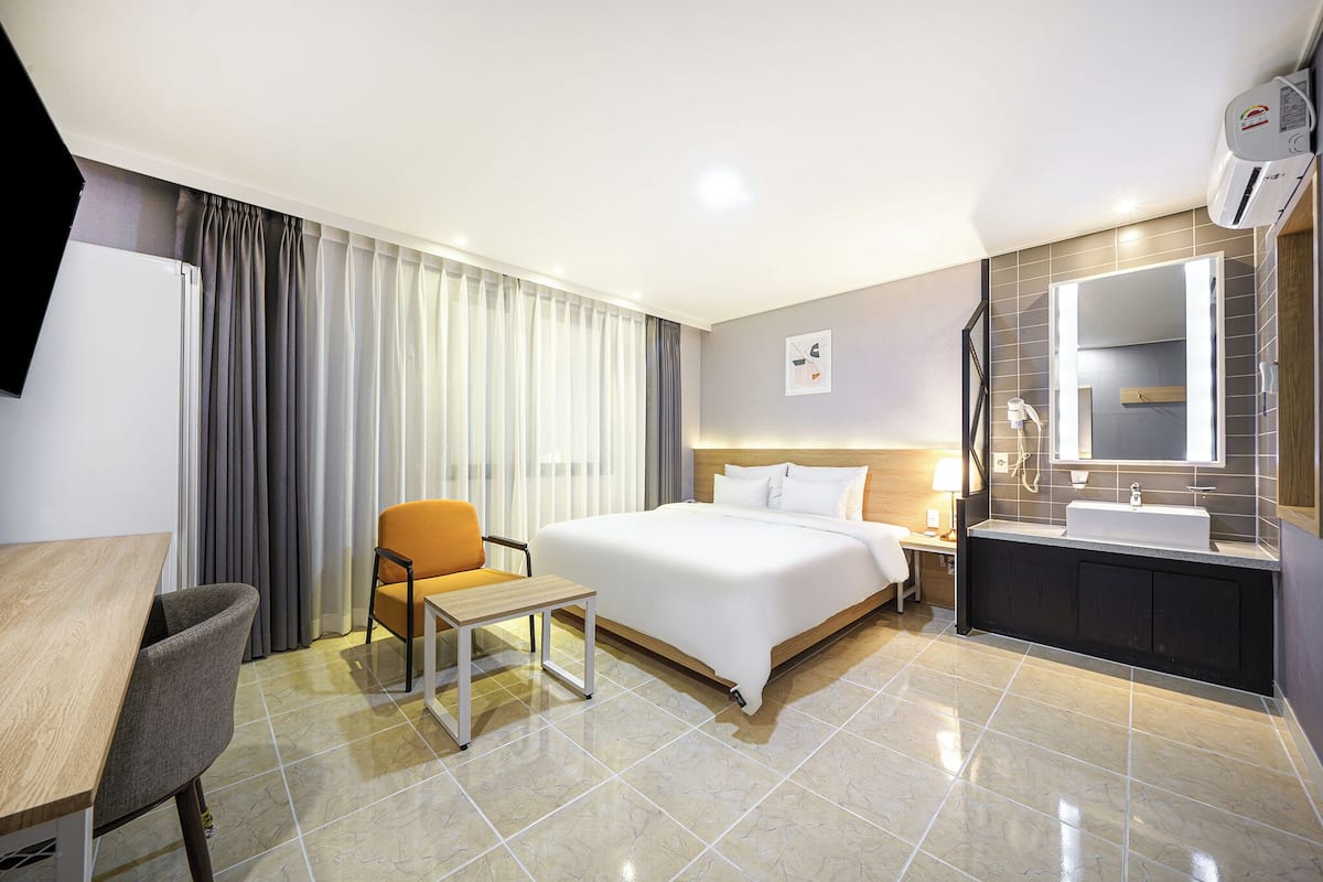 A hotel room with a bed, a desk, a chair, a bathroom with a sink and mirror, and curtains.
