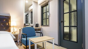 A hotel room with a bed, a desk with a chair, a small table, a mirror, and a door with frosted glass panels. - Browndot Angang (Gyeongju)