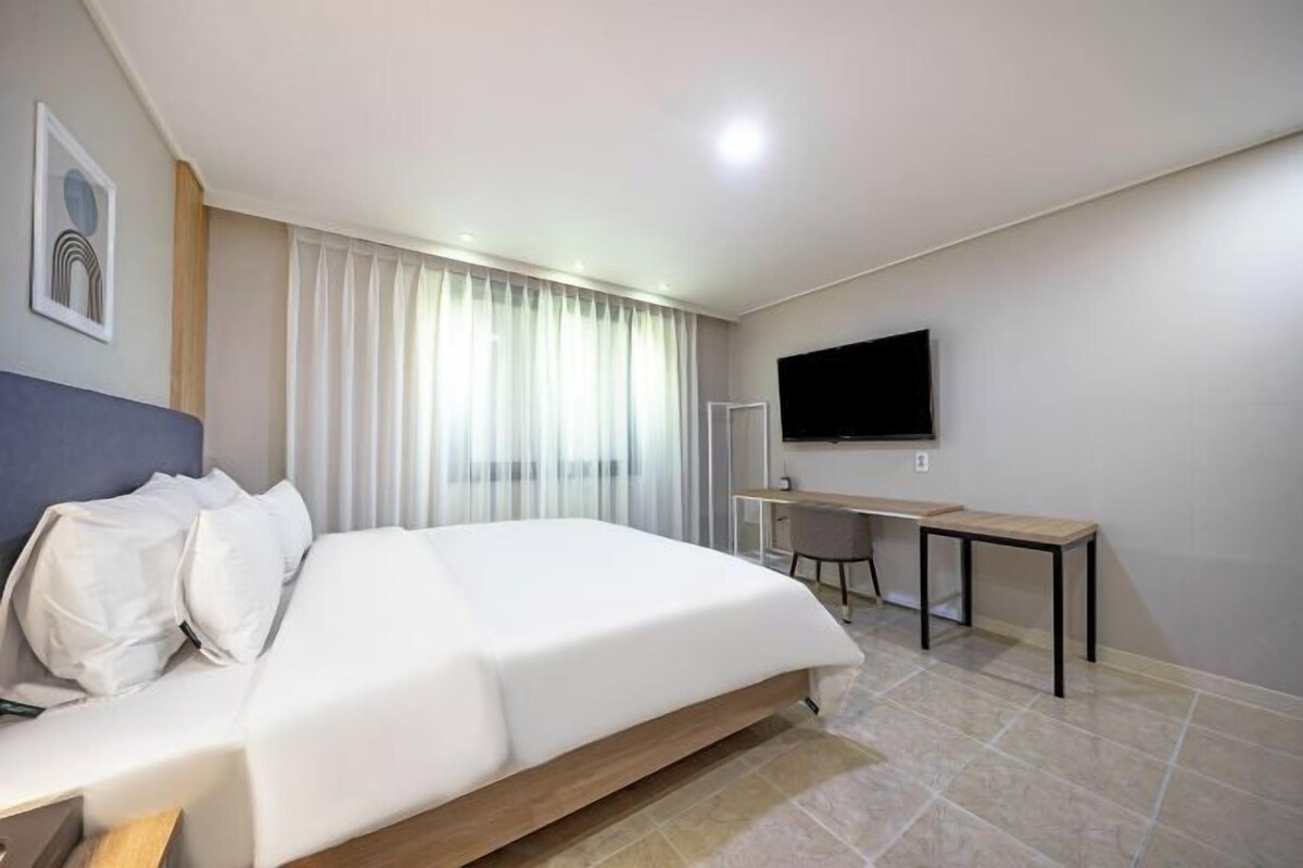 A modern hotel room with a large bed, a desk, and a TV.