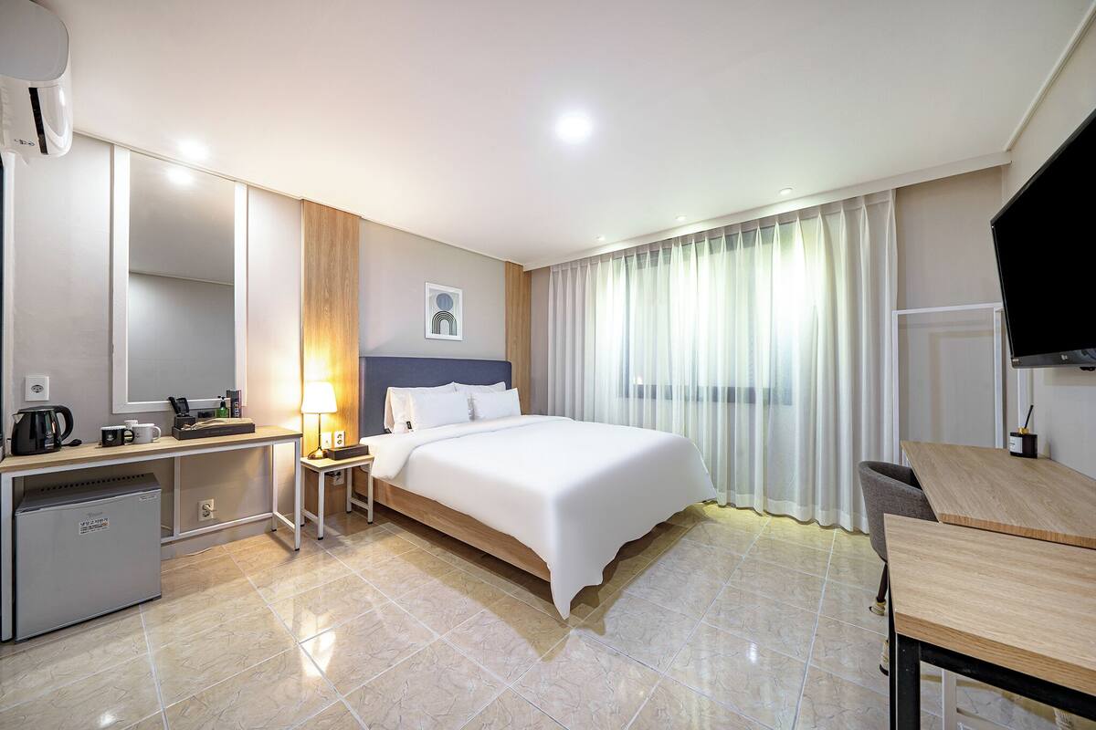 A hotel room with a bed, a desk, a chair, a TV, and a minibar.