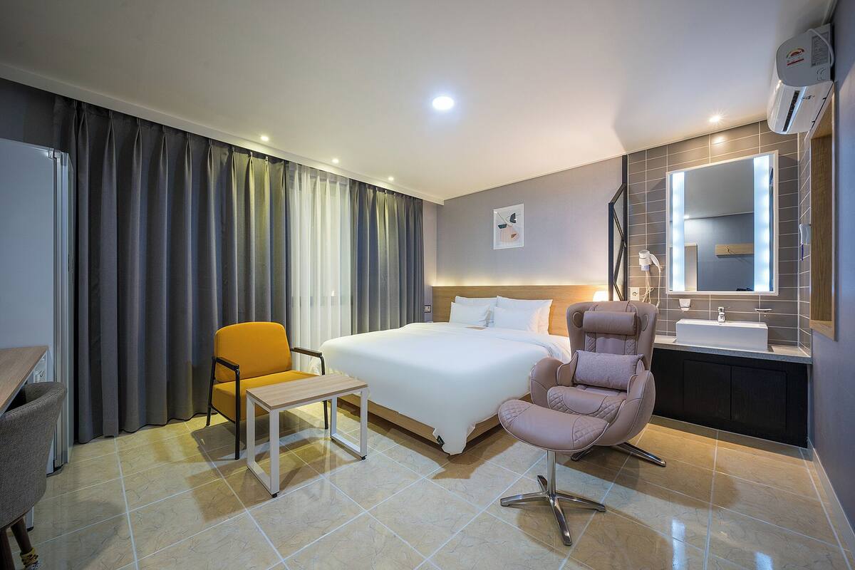 A hotel room with a bed, a desk, a chair, a sofa, a mirror, and a sink.
