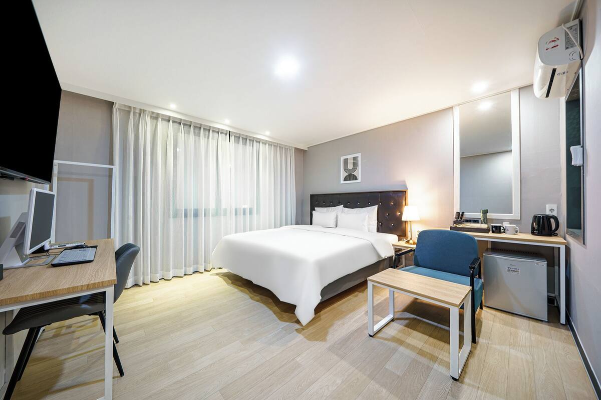 A hotel room with a bed, desk, chair, and a small refrigerator.