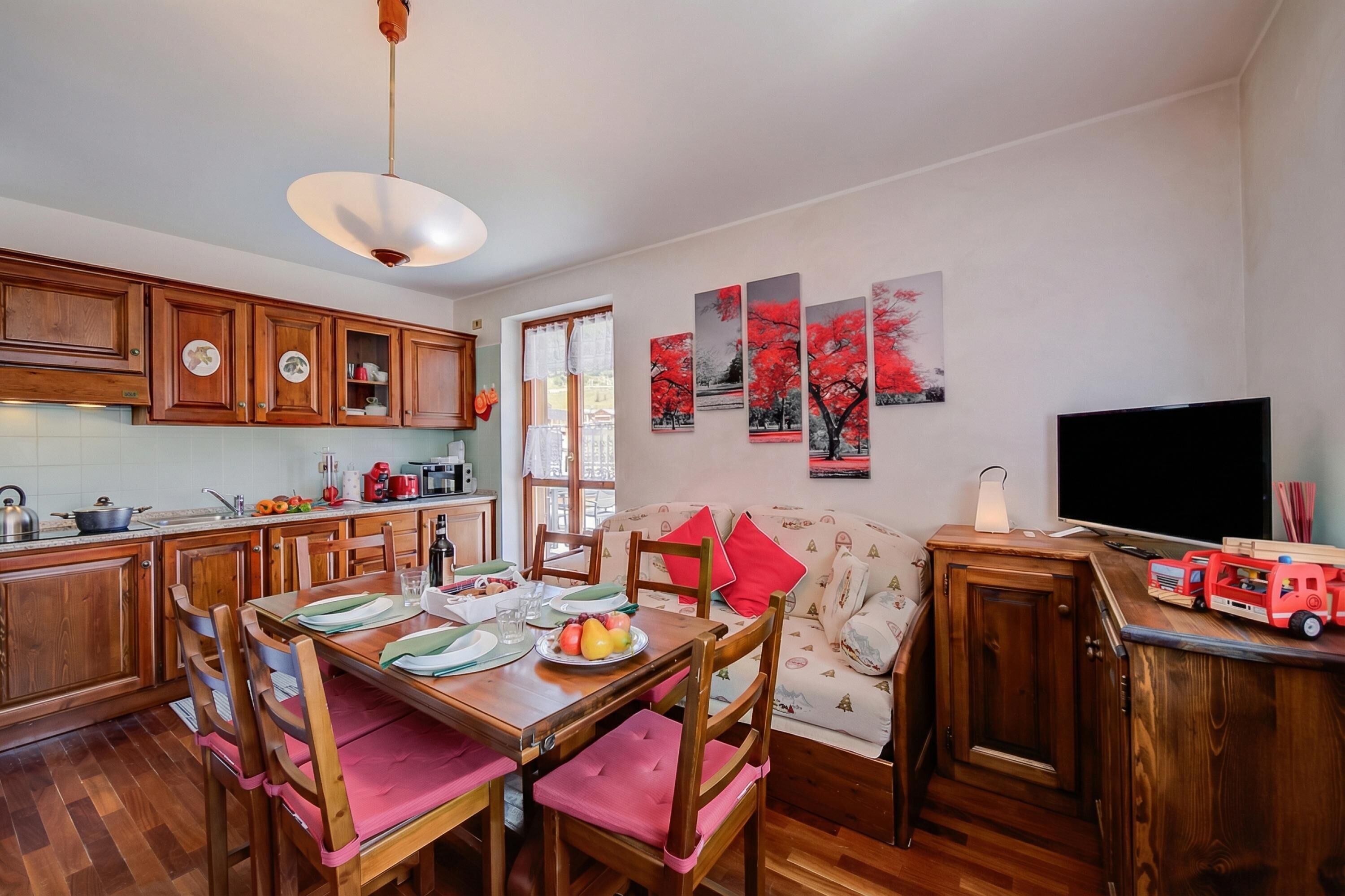 Un coin repas avec des meubles en bois, une table dressée avec des assiettes et des verres, et un canapé à motifs rouges et blancs.