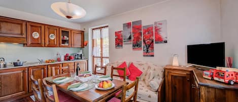 A dining area with wooden furniture, a table set with plates and glasses, and a red and white patterned sofa.