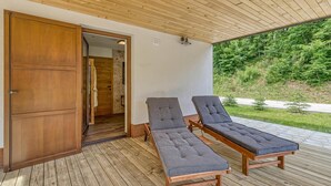 Una terraza de madera con dos sillones de descanso y una puerta de madera que da a un espacio interior.