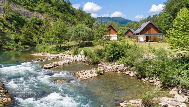 Un río serpentea por una zona boscosa con dos cabañas de madera.