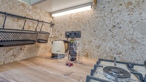 Una cocina con estufa a gas, un hervidor, una botella de vino y una copa de vino.