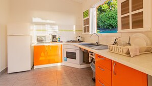 A kitchen with white and orange cabinets, a microwave, oven, sink, and a window with a view of greenery.