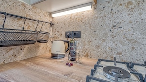 A kitchen with a gas stove, a kettle, a wine bottle, and a wine glass.