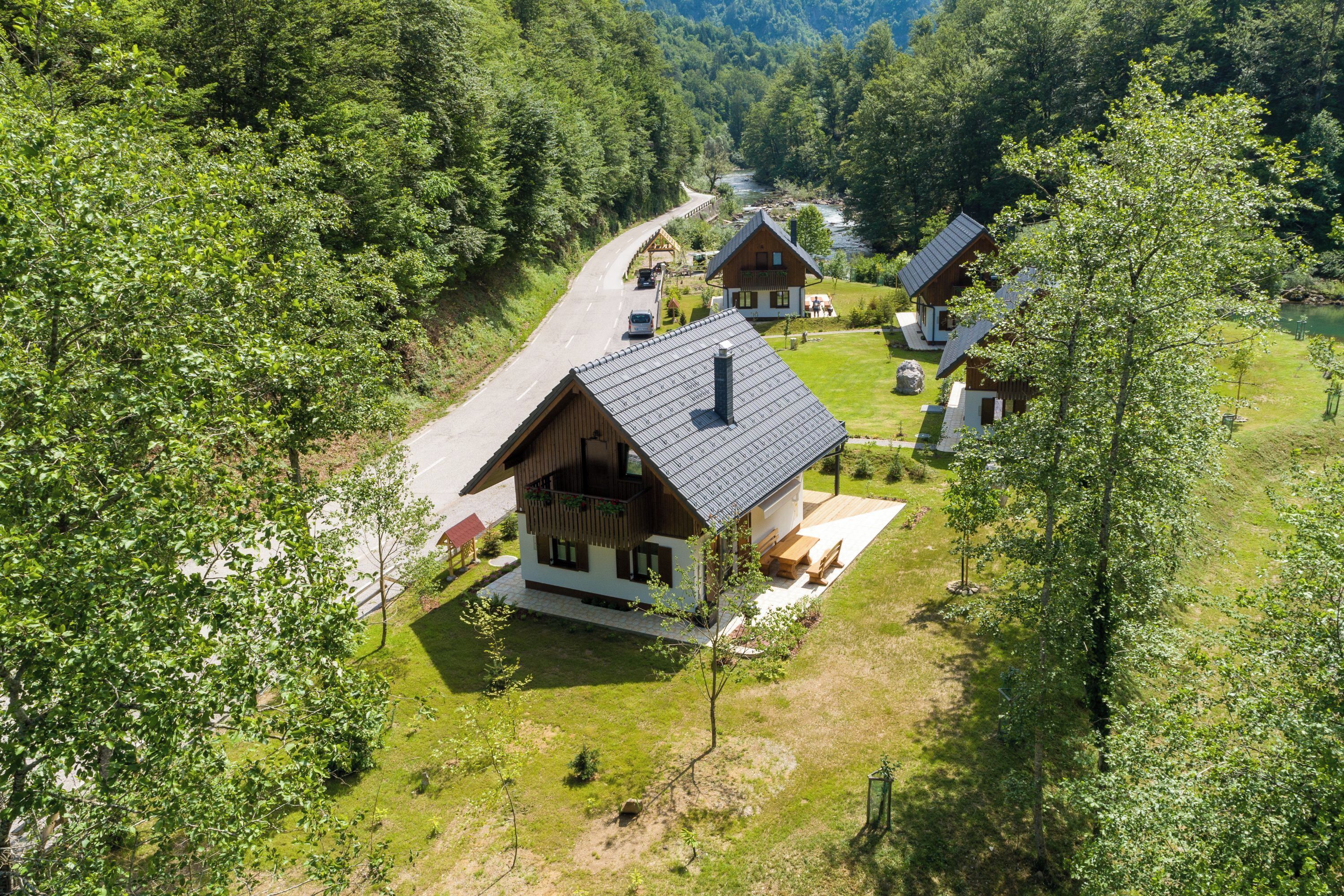 A wooden cabin with a sloped roof, surrounded by lush greenery and a winding road.