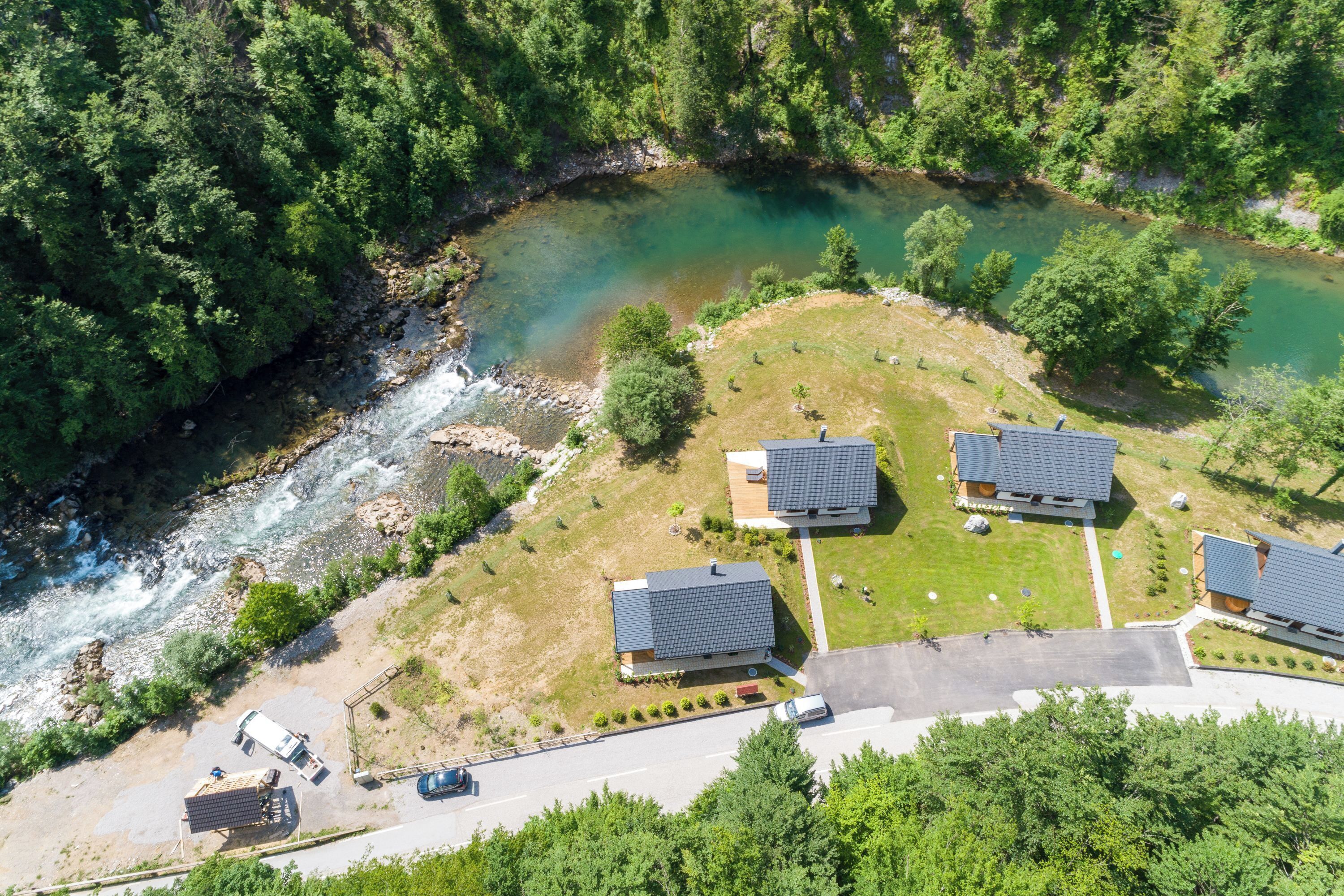 An aerial view of a residential area with three houses, a river, and a road.