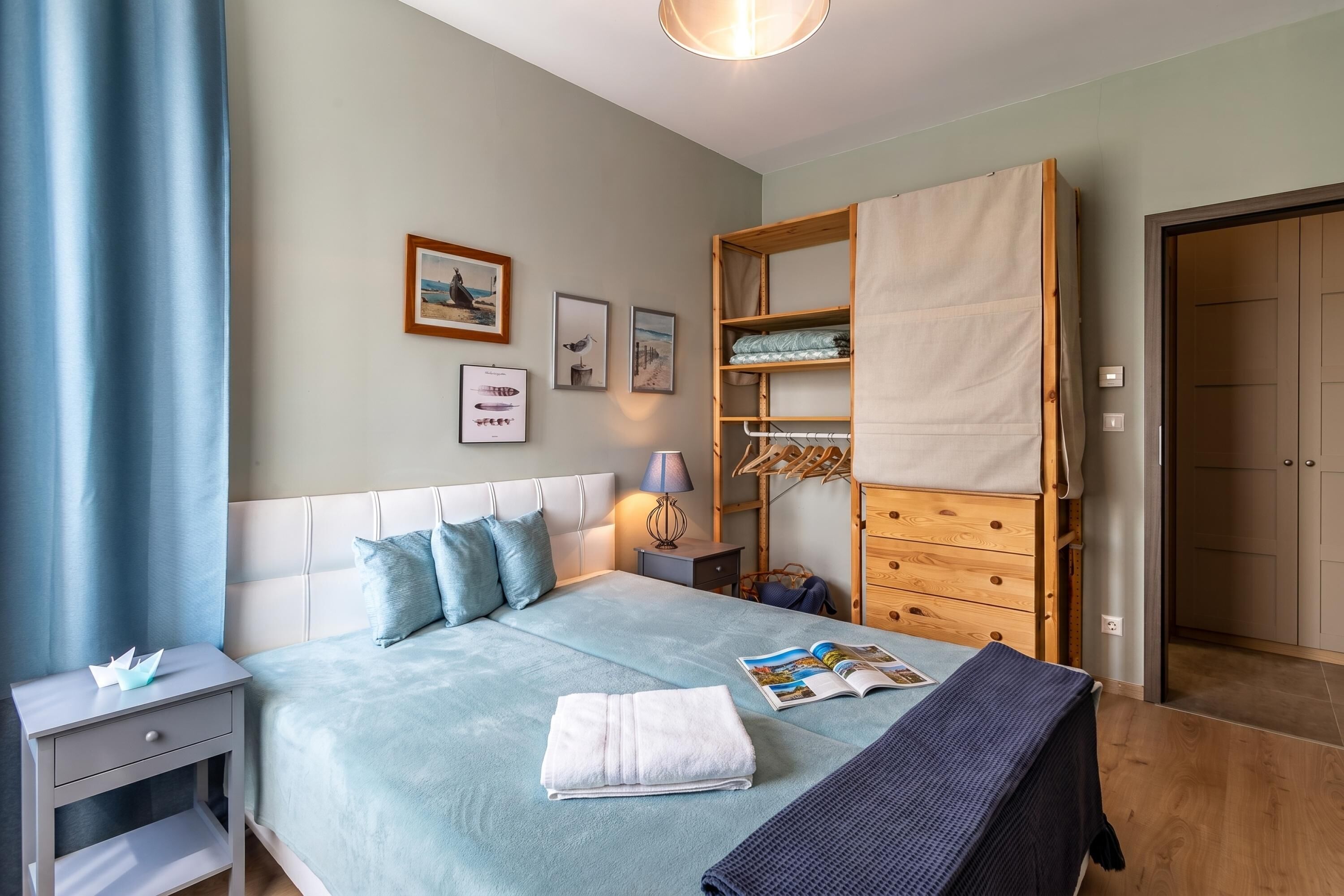 Un lit bien fait, avec des oreillers, une table de chevet avec une lampe, une armoire en bois et un mur orné de tableaux encadrés.