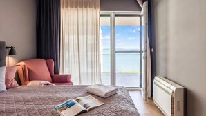Ein Hotelzimmer mit Bett, Leselampe, Sessel, Fenster mit Vorhängen und Heizkörper.