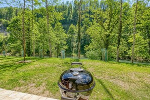 Una parrilla para barbacoa en un espacio al aire libre con césped, árboles y un cuerpo de agua al fondo.