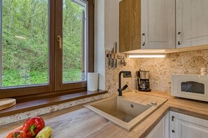 A kitchen with a large window, wooden cabinets, a sink, and a microwave.