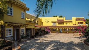 A courtyard with yellow buildings, stone paving, and potted plants. - Hacienda Girasoles Tampico (Pueblo Viejo)