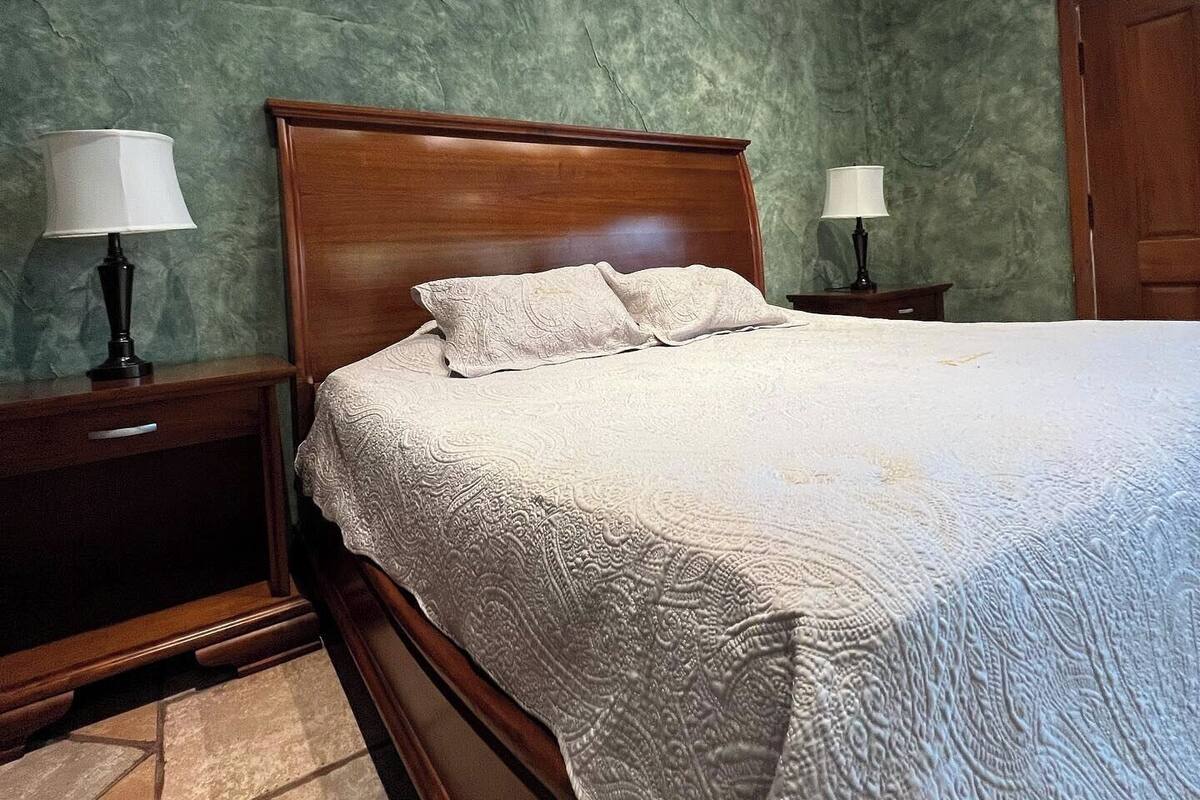 Une chambre à coucher avec un lit en bois, des murs verts à texture et deux lampes de chevet.