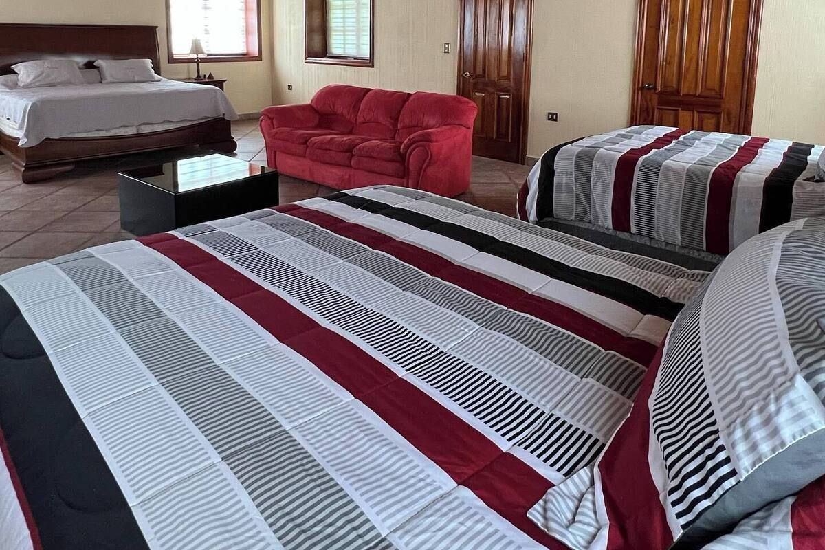 Une pièce avec un grand lit, un canapé rouge et deux portes.