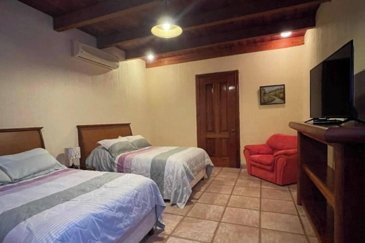Une chambre avec deux lits, un téléviseur, un fauteuil rouge et un plafond en bois.