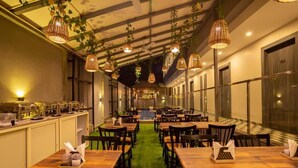 A restaurant with wooden tables, hanging wicker lamps, and a green carpeted floor. - The Porto by Lagom (Vagator)