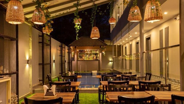 An outdoor dining area with tables and chairs, hanging wicker lamps, and a bar in the background. - The Porto by Lagom (Vagator)