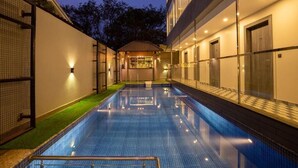 A swimming pool with a tiled floor, surrounded by a building with a glass facade and a small outdoor bar area. - The Porto by Lagom (Vagator)