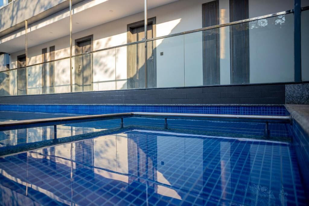 A swimming pool with clear blue tiles, a glass railing, and a building with windows in the background.